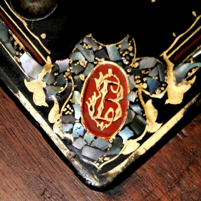Nahaufnahme einer kunstvollen, dekorativen Oberflächengestaltung mit einem roten Monogramm und Goldverzierungen.