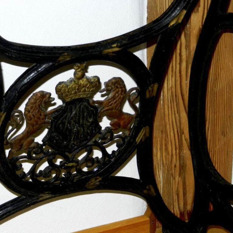 Ornamentales schwarzes Schmiedeeisengestell mit einem zentralen, detaillierten Relief von Tieren und einer Krone.