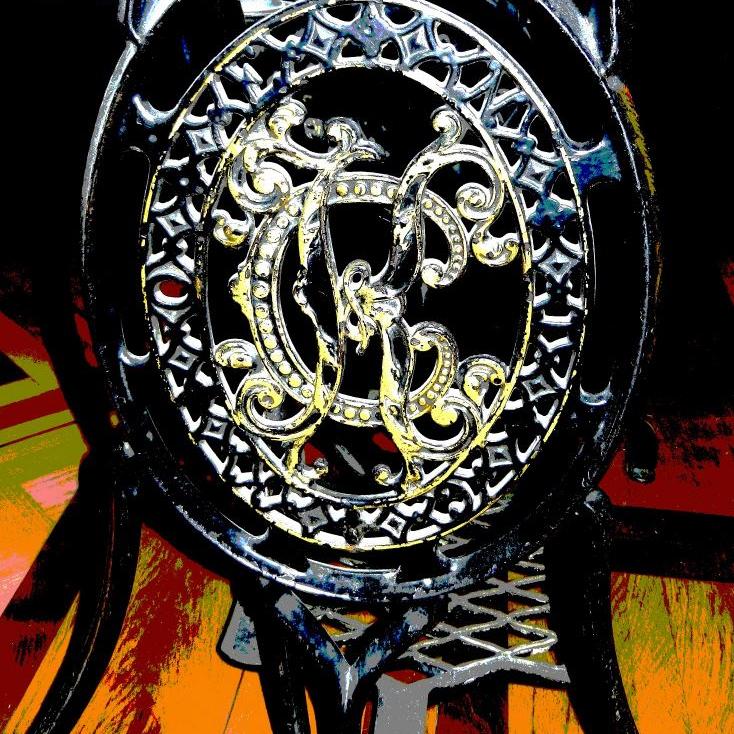 Detailaufnahme von kunstvollem, geschwungenem Metallornament in Form eines Medillons.