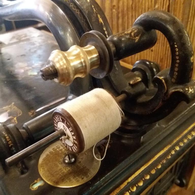 Nahaufnahme einer antiken Nähmaschine mit Spulen und Metallkomponenten.