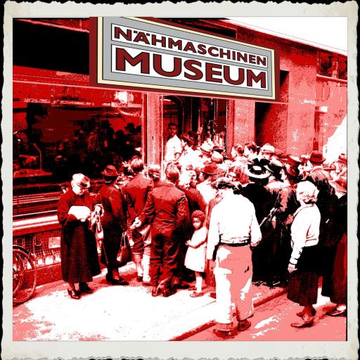 Eine historische Aufnahme zeigt eine große Gruppe von Menschen, die in einem Museum, das Nähmaschinen ausstellt, zusammengekommen sind.