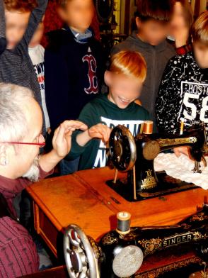 Eine Gruppe von Kindern steht um eine historischen Nähmaschine.