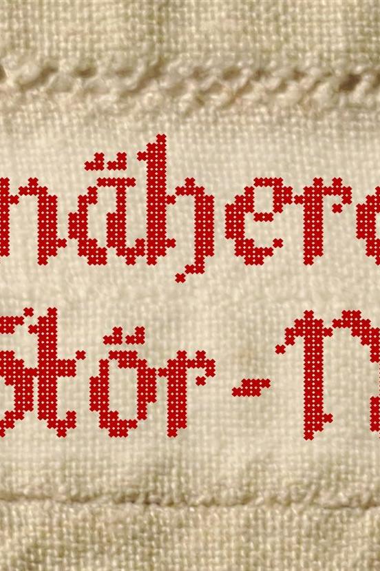 Gestickte Schrift auf weißem Tuch, die die Wörter Weissnäherei und Stör-Näherei zeigt.